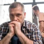 Man contemplating internalized homophobia with his partner looking upset behind him