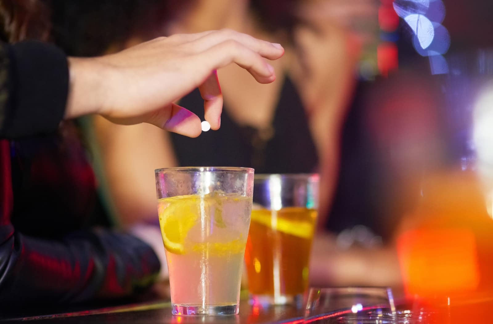 man dropping drugs into drinks at a bar - signs of being roofied