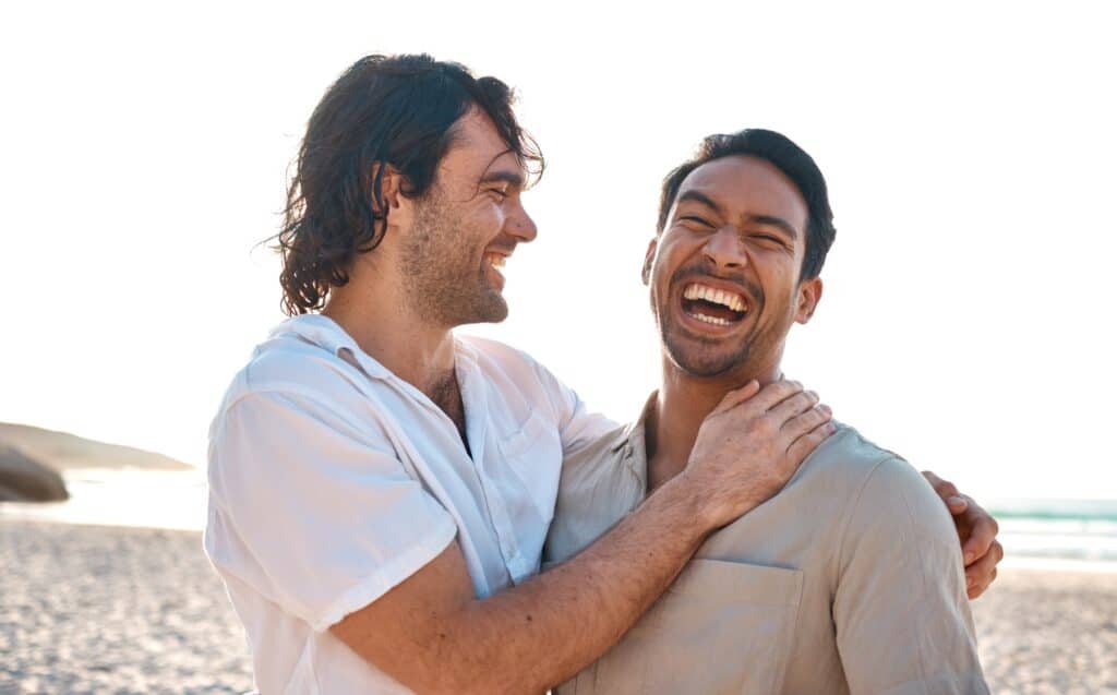 gay couple laughing and smiling on a beach in los angeles