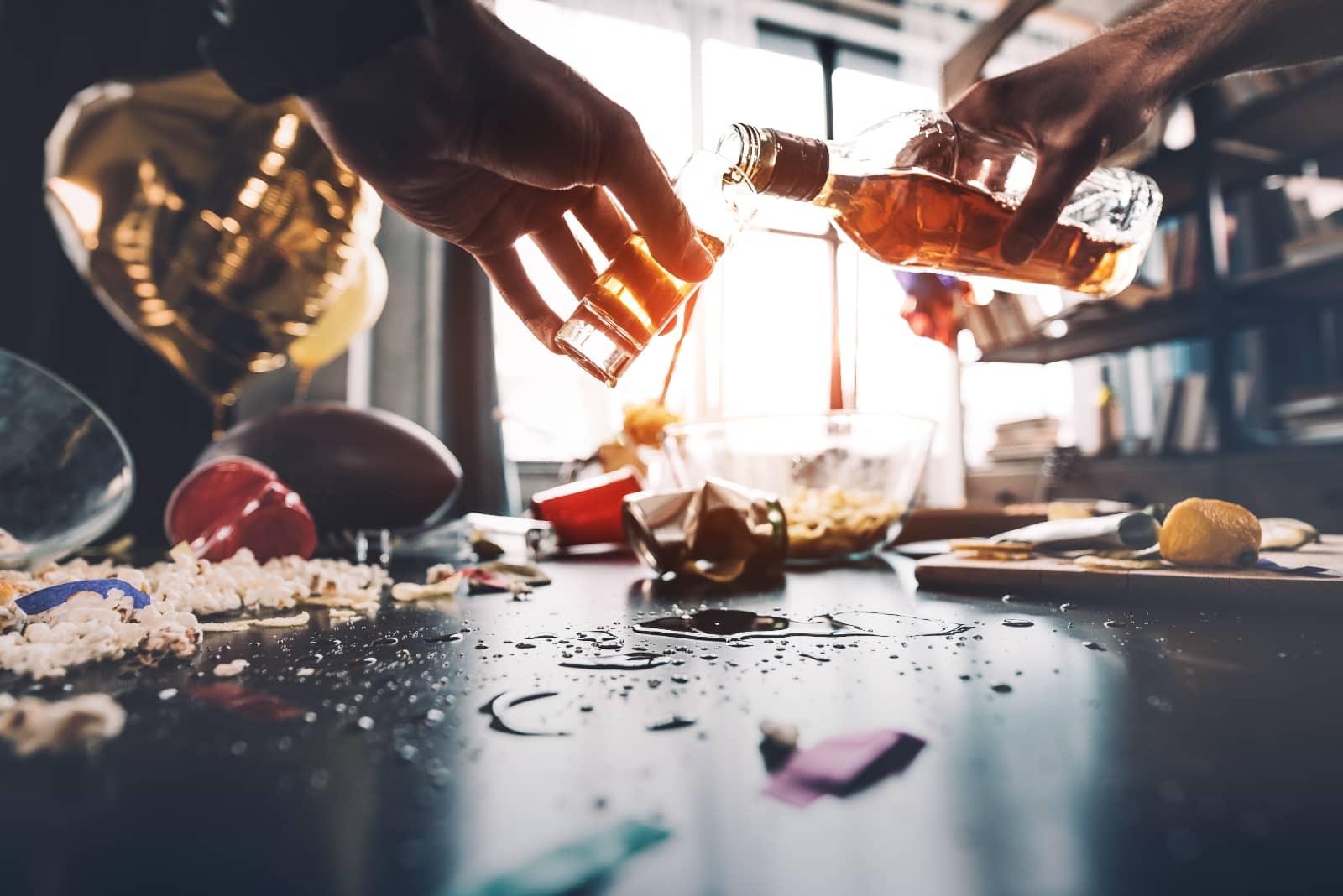 close up of person pouring alcohol on a table filled with cups and party drugs