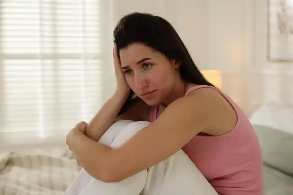 LGBTQ+ adult sitting in bed as they consider the connection between PTSD and addiction and consider trauma-informed care