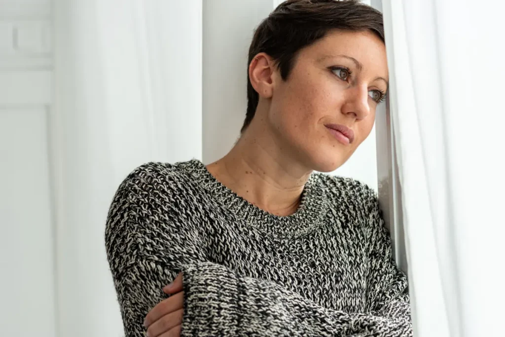 Thoughtful bisexual adult sitting alone by a window, reflecting on substance use recovery and the impact of erasure