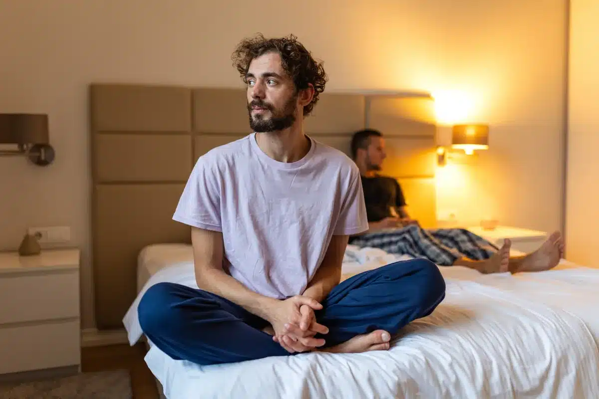 Person sitting on bed with man behind, reflecting on chemsex and crystal meth recovery through CSAT-led treatment