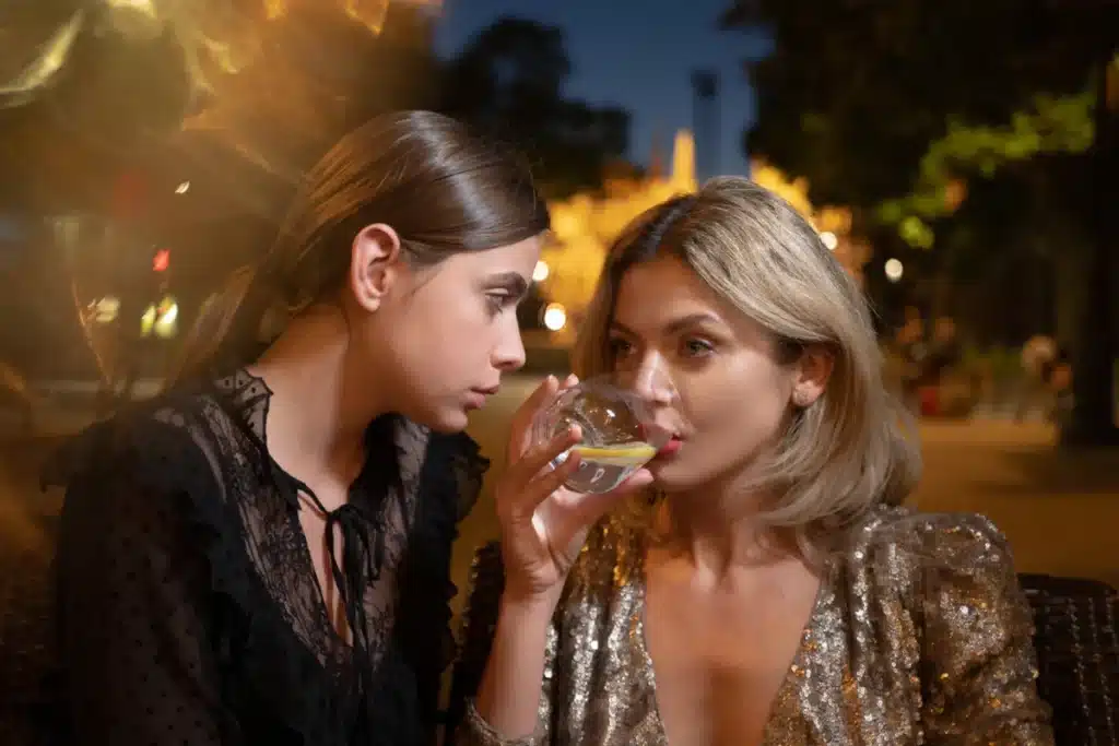 One queer woman looking at another drinking at a party, reflecting lesbian women's higher alcohol risk and affirming recovery
